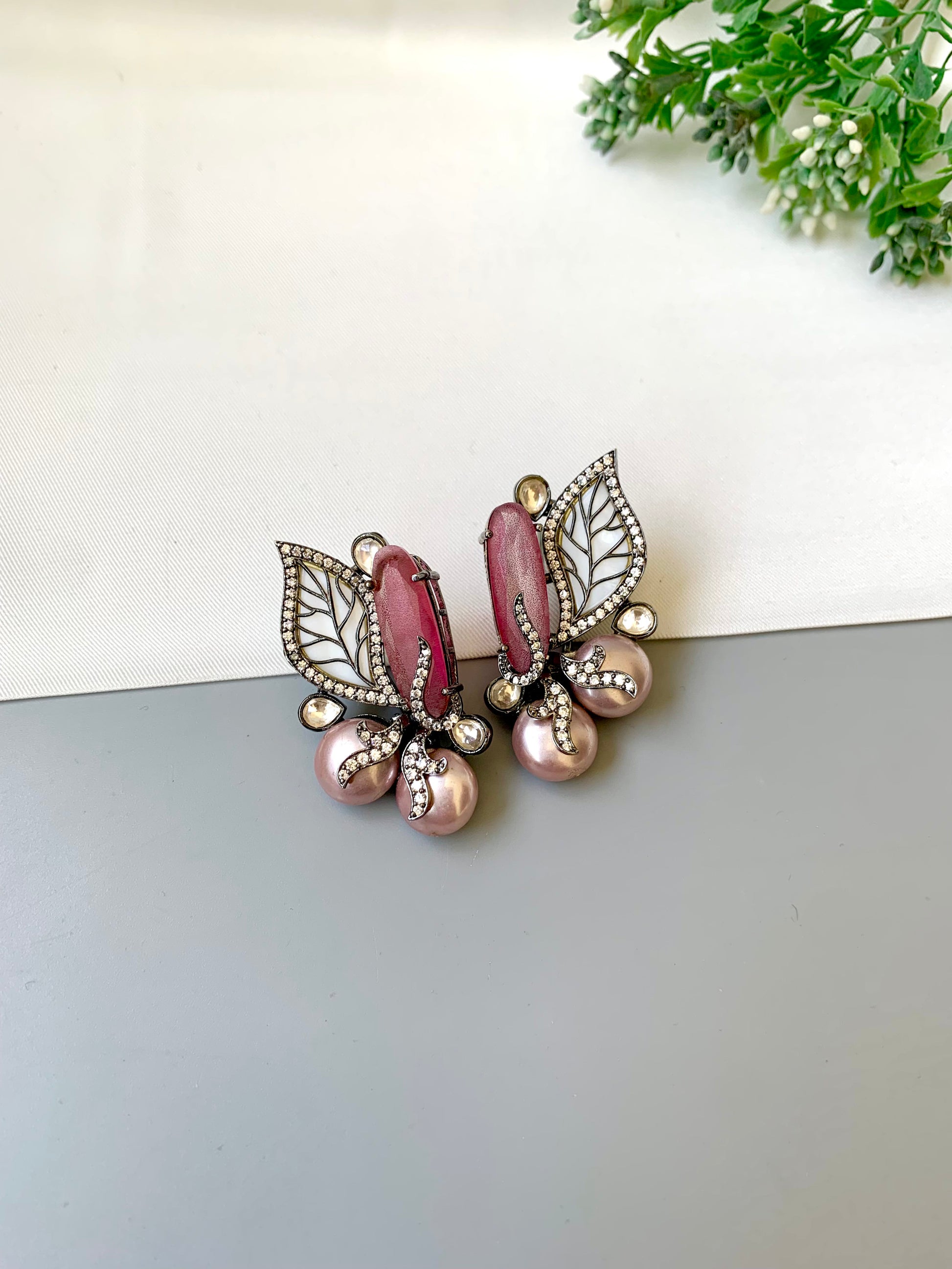 Pair of earrings with pink gemstones and leaf designs on a white surface.