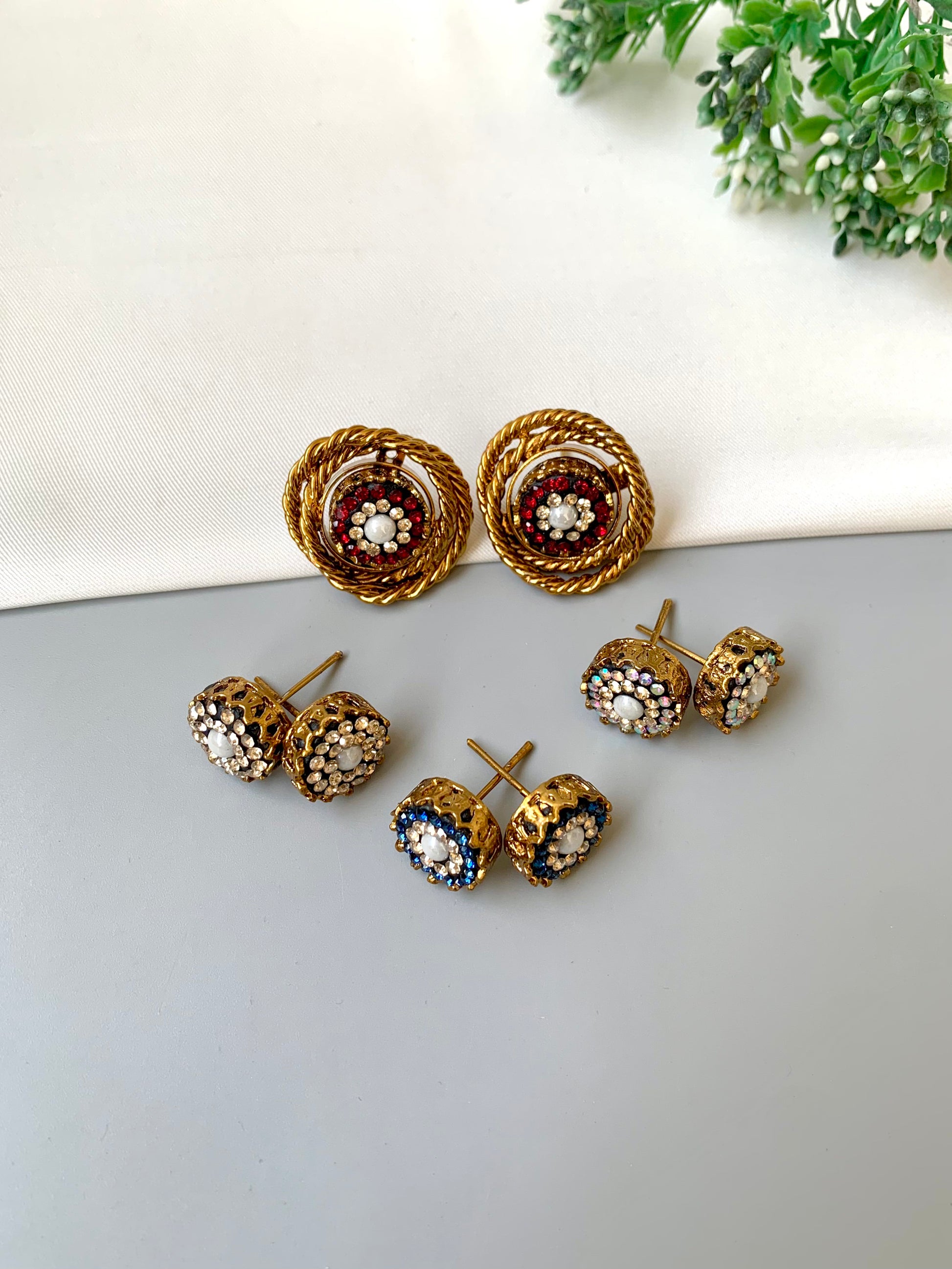 Set of gold earrings with gemstones on a light gray surface with greenery in the background