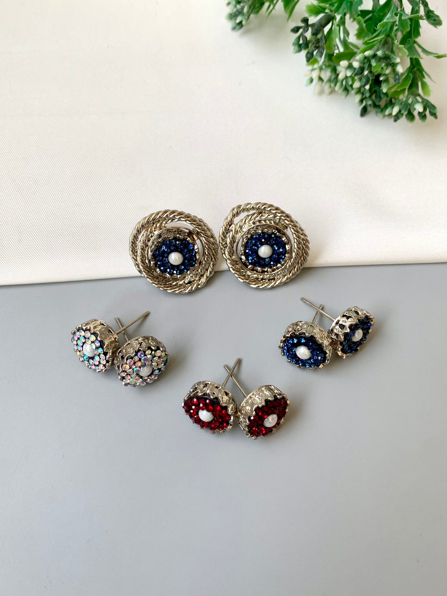 Set of earrings on a light gray surface with greenery in the background