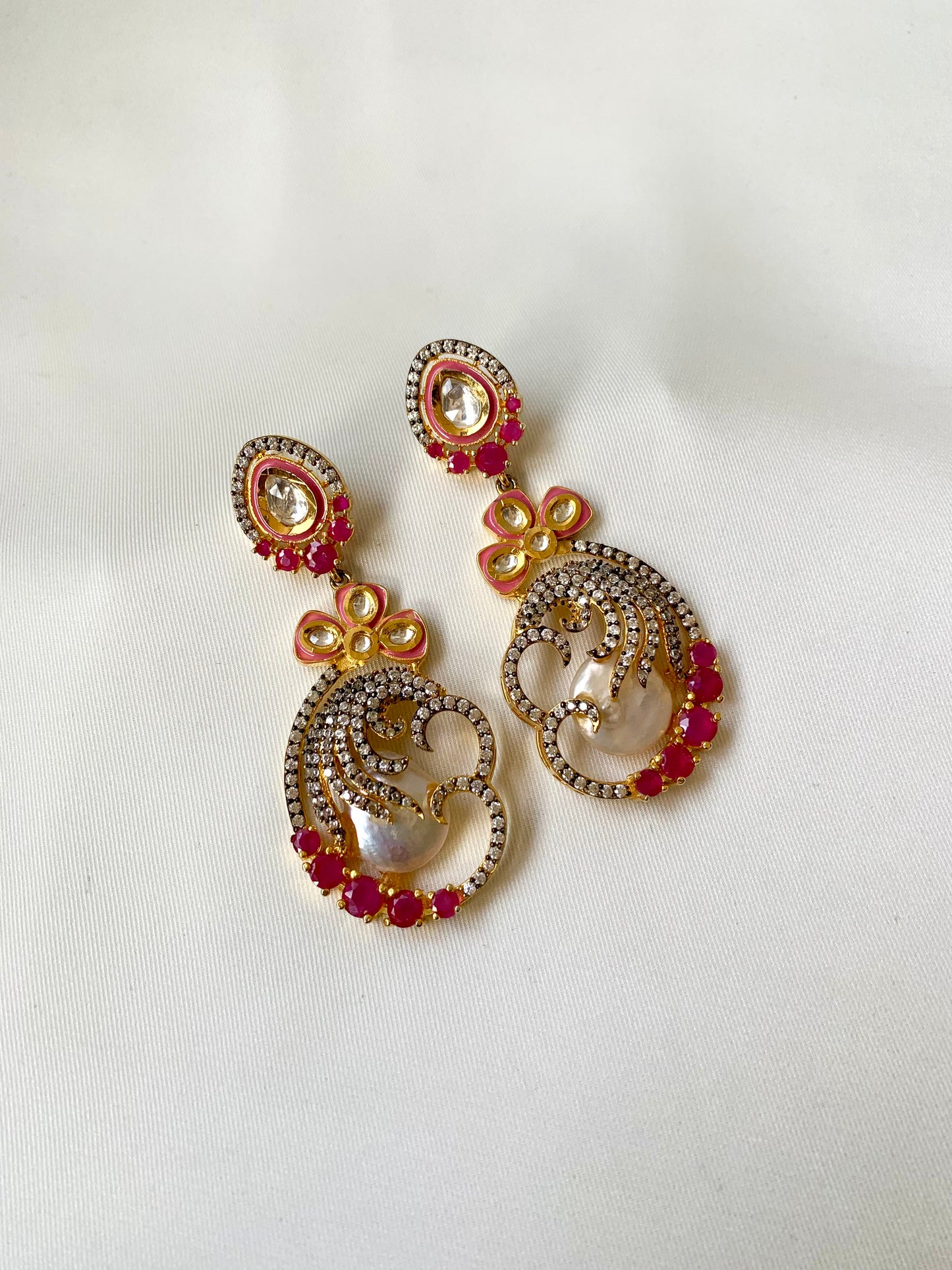 Ornate earrings with circular designs and red gemstones on a white background