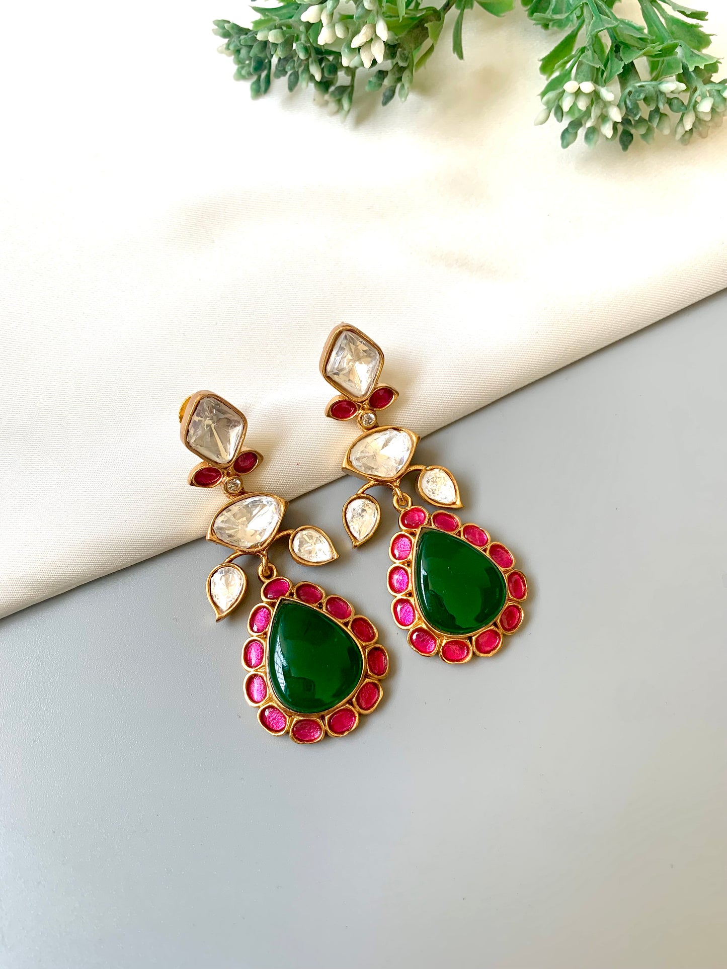 Gold earrings with green and red stones on a light background