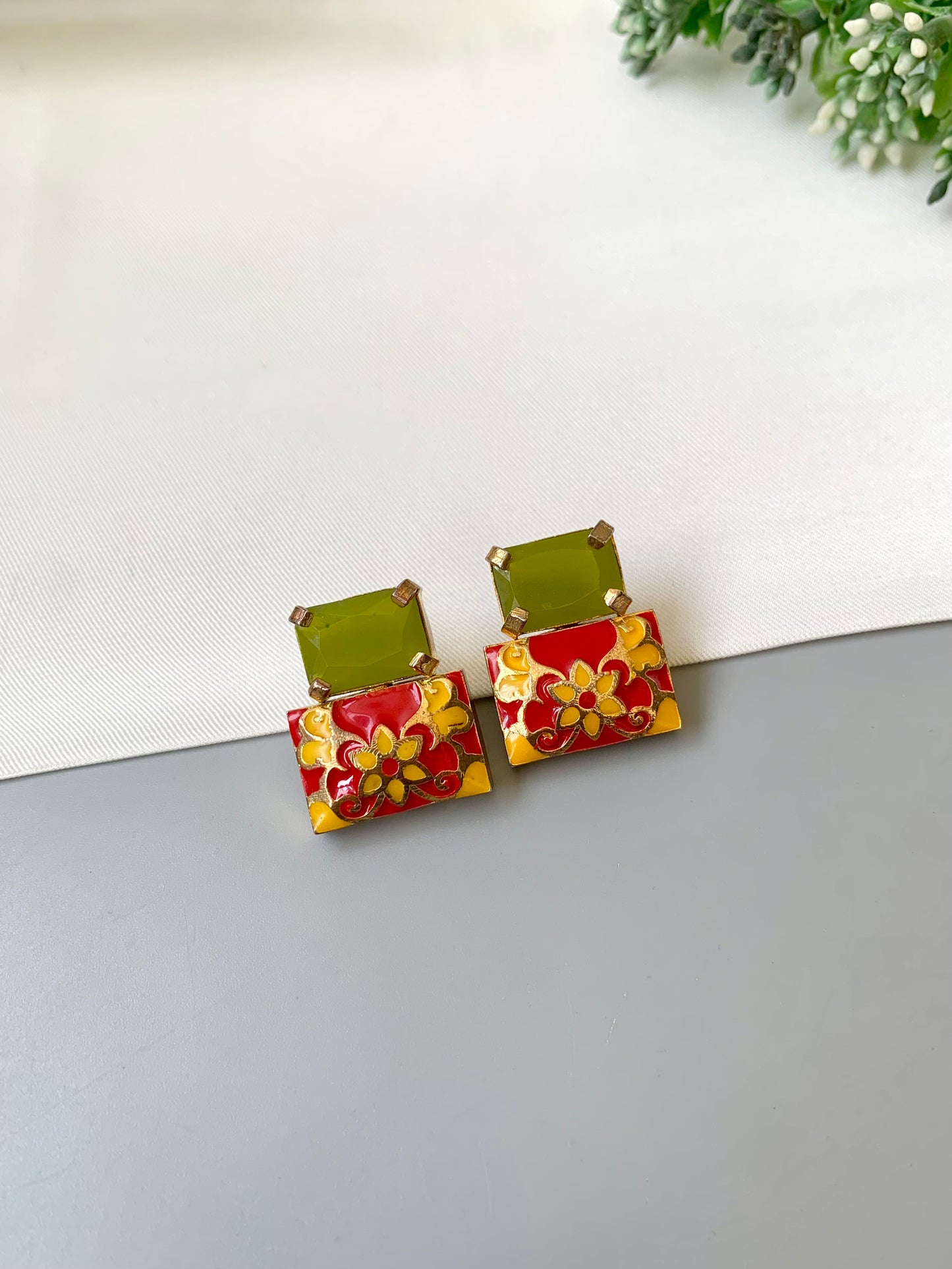 Pair of earrings with green and red floral designs on a light gray surface.