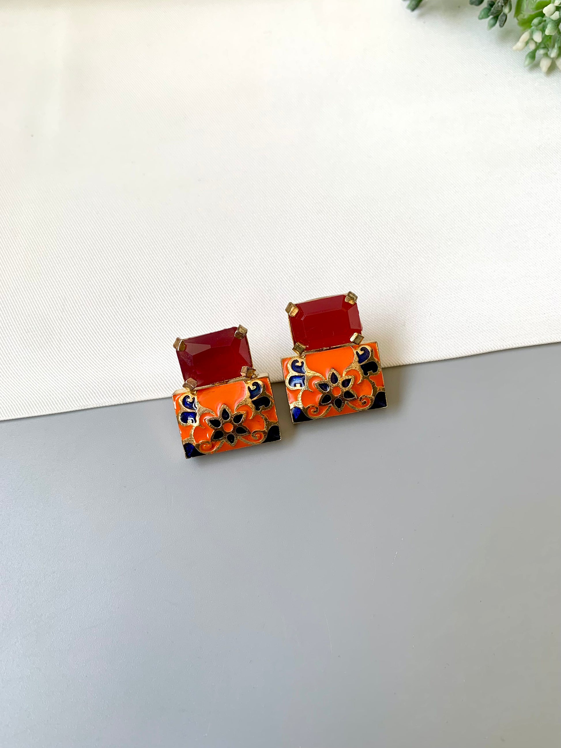 Pair of earrings with red and orange square designs on a white surface