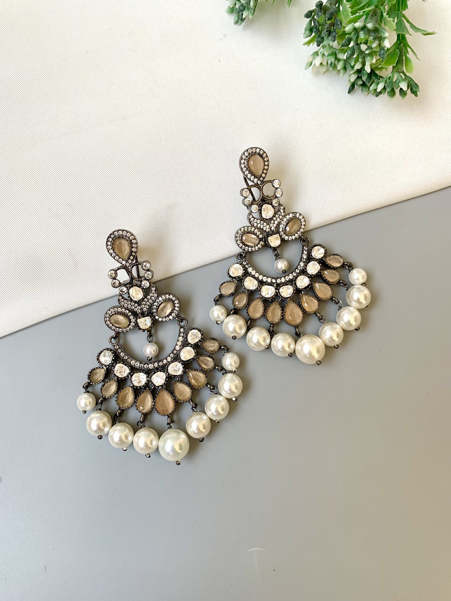 Pair of ornate earrings with pearls on a light surface.