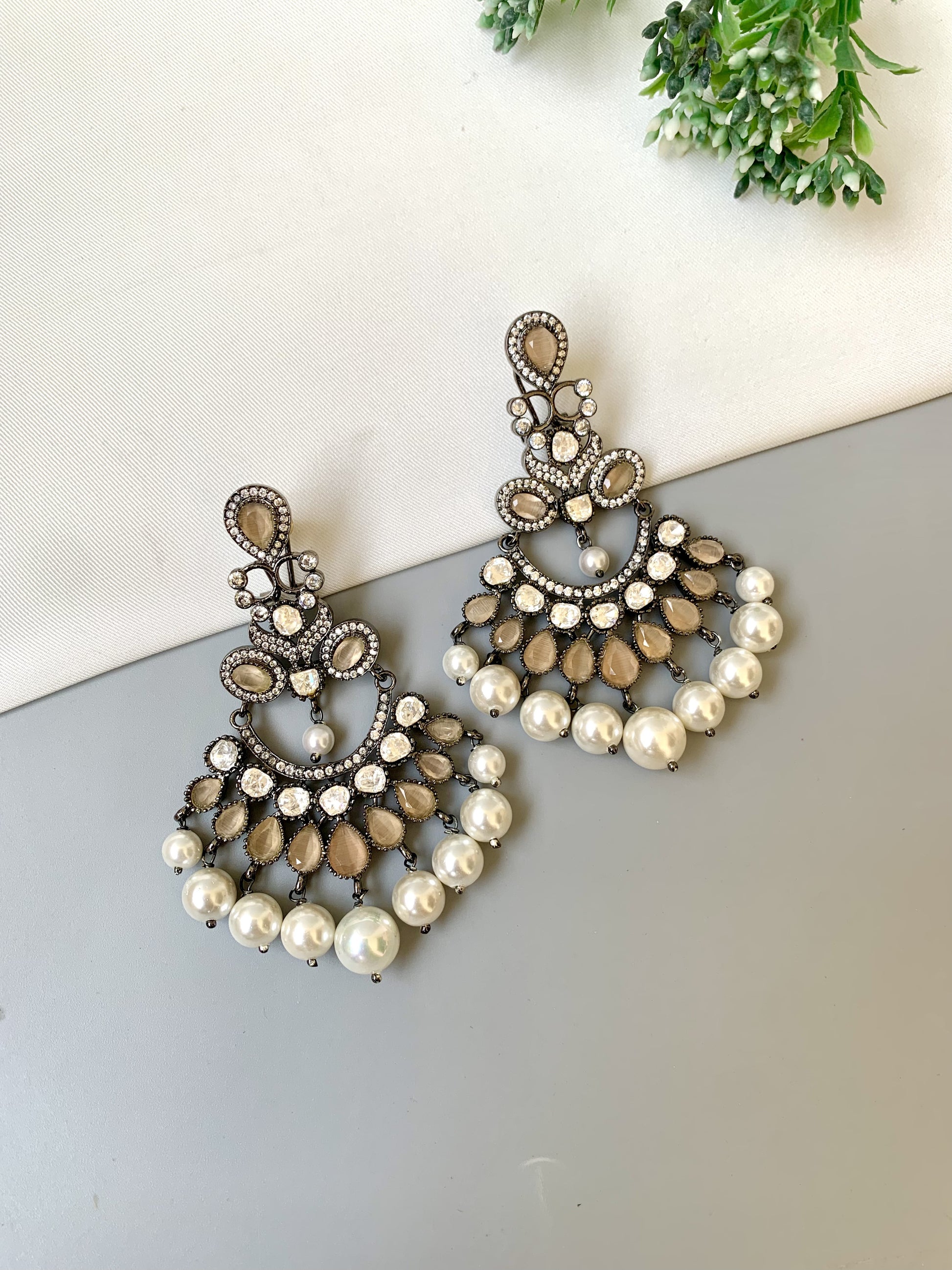 Pair of ornate earrings with pearls on a light surface.