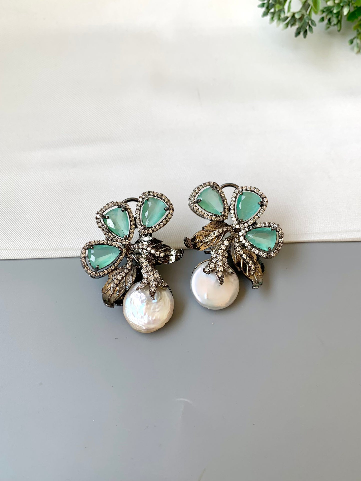 Pair of earrings with green gemstones and pearls on a white surface.