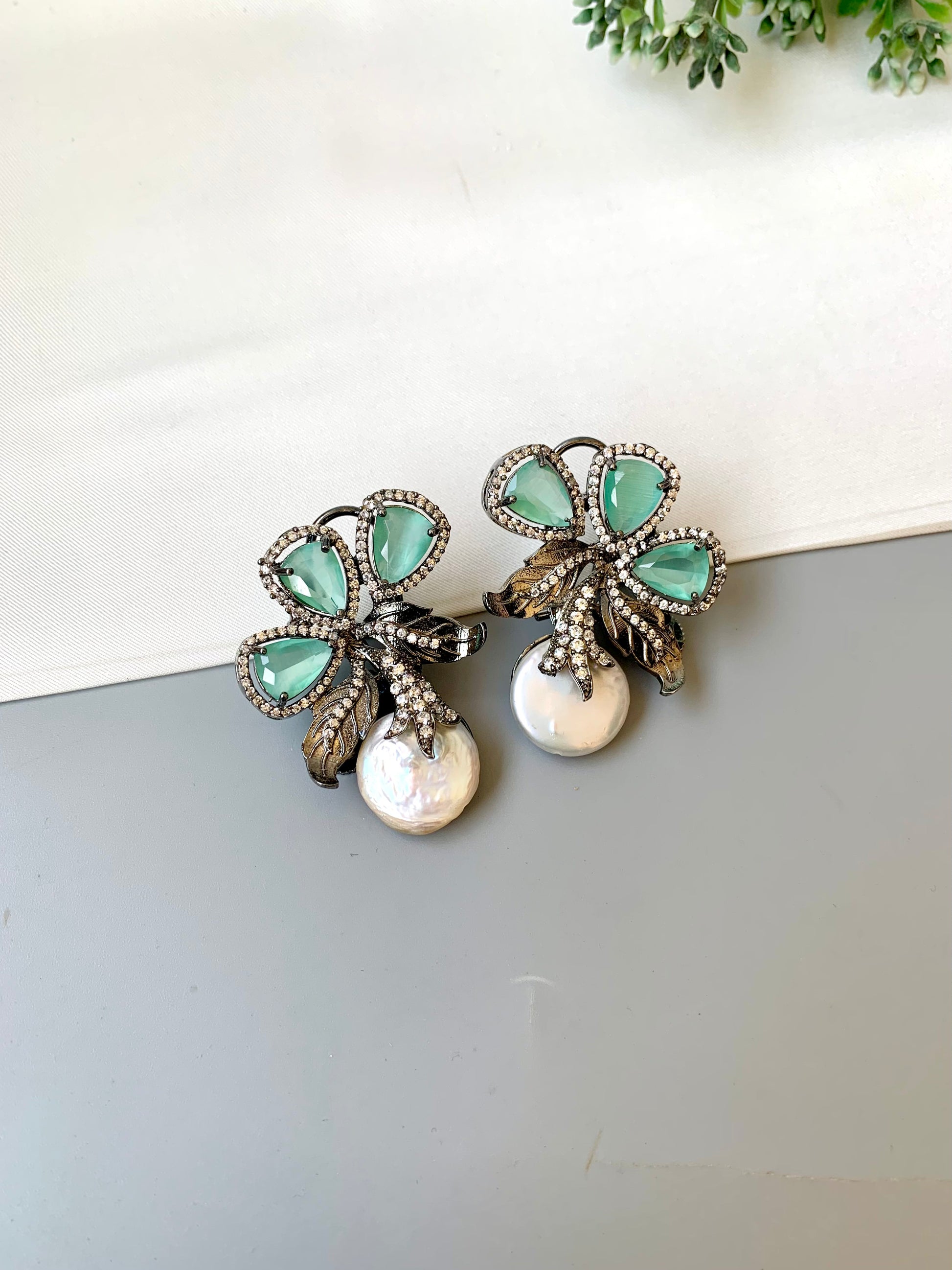 Pair of earrings with green gemstones and pearl-like elements on a white surface.