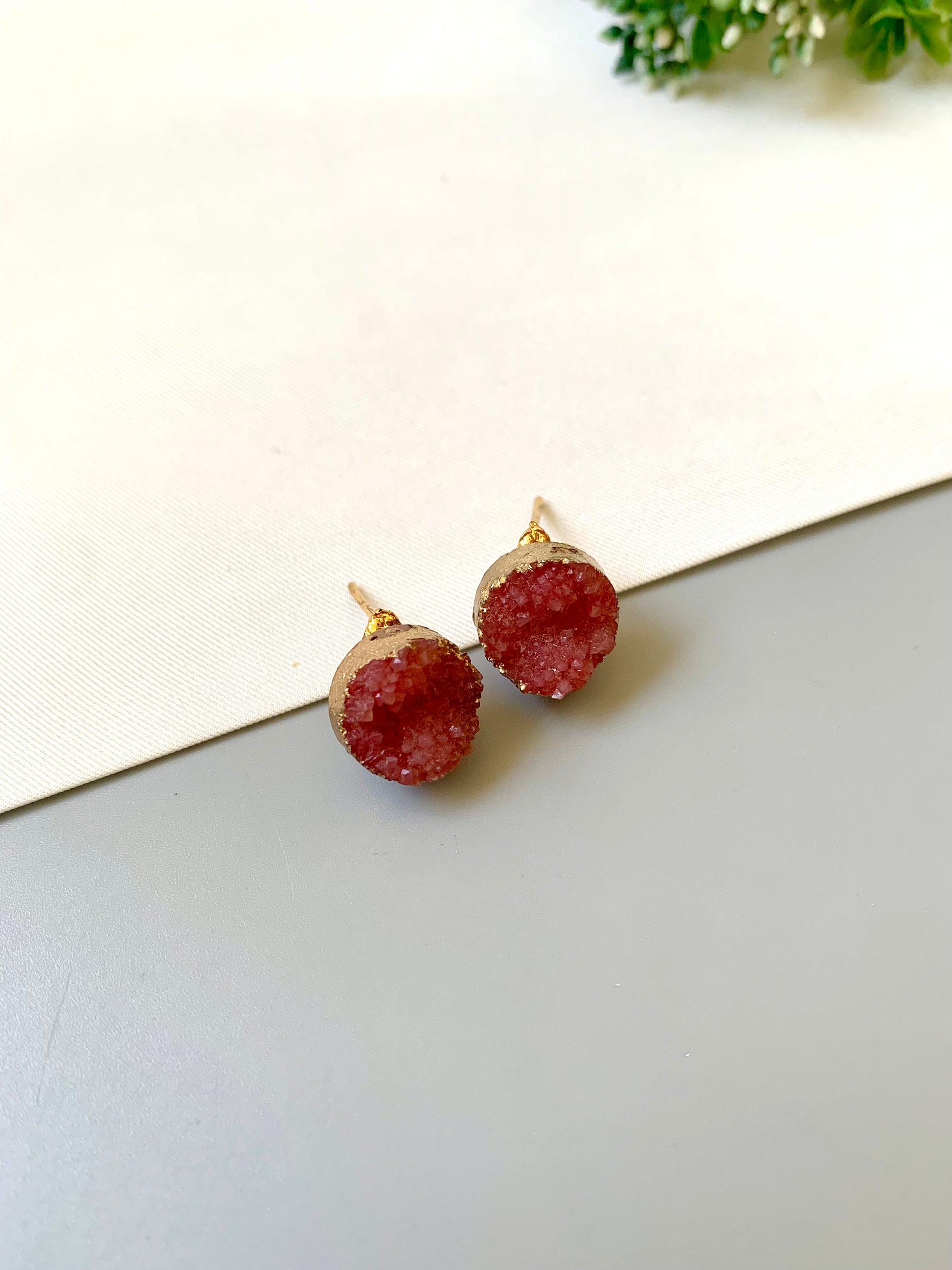 Pair of red druzy stud earrings on a light surface with a white background