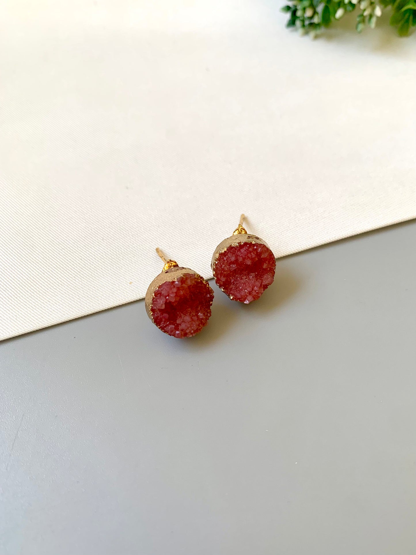 Pair of red druzy earrings on a light gray surface with a white background