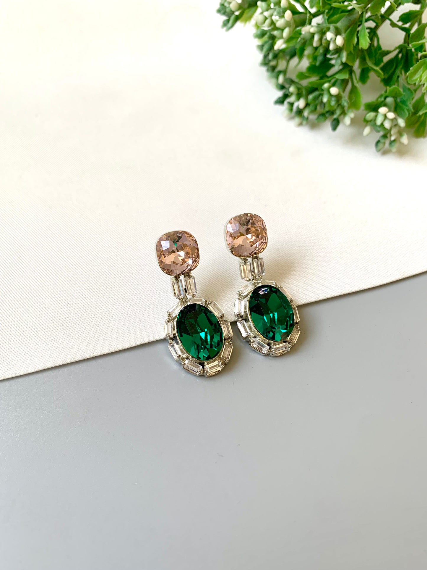 Pair of earrings with green gemstones on a light surface with greenery in the background