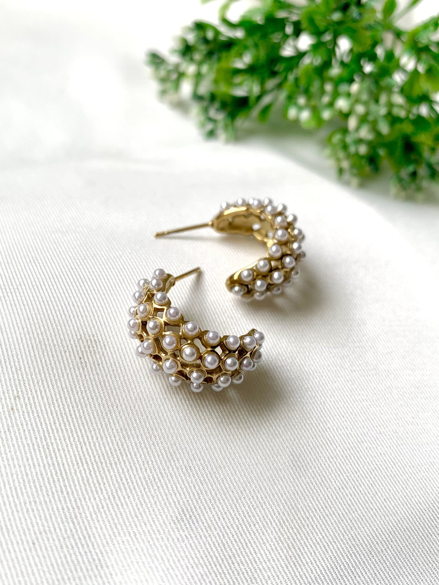 Pair of gold hoop earrings with pearls on a white surface with greenery in the background