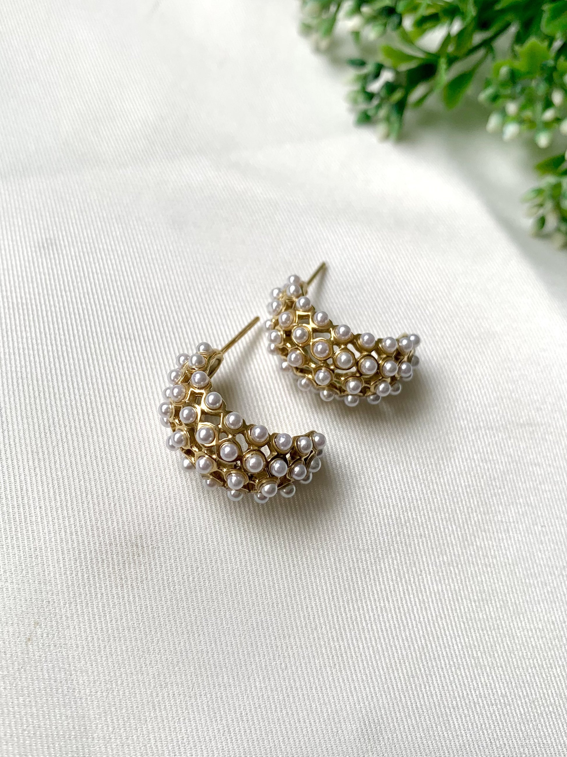 Gold hoop earrings with pearl accents on a white surface with greenery in the background