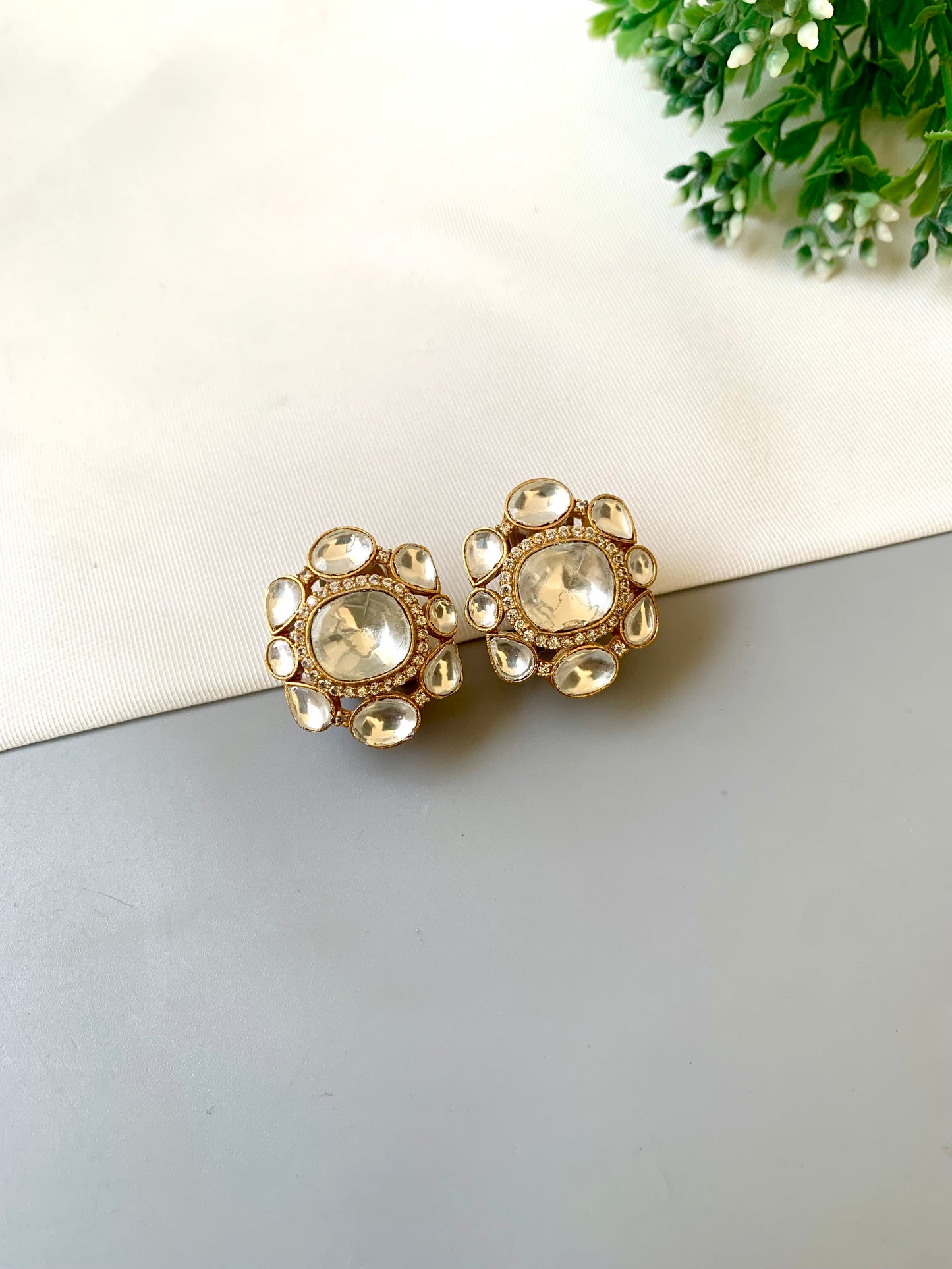 Gold and pearl earrings on a light gray surface with a white card and green leaves in the background