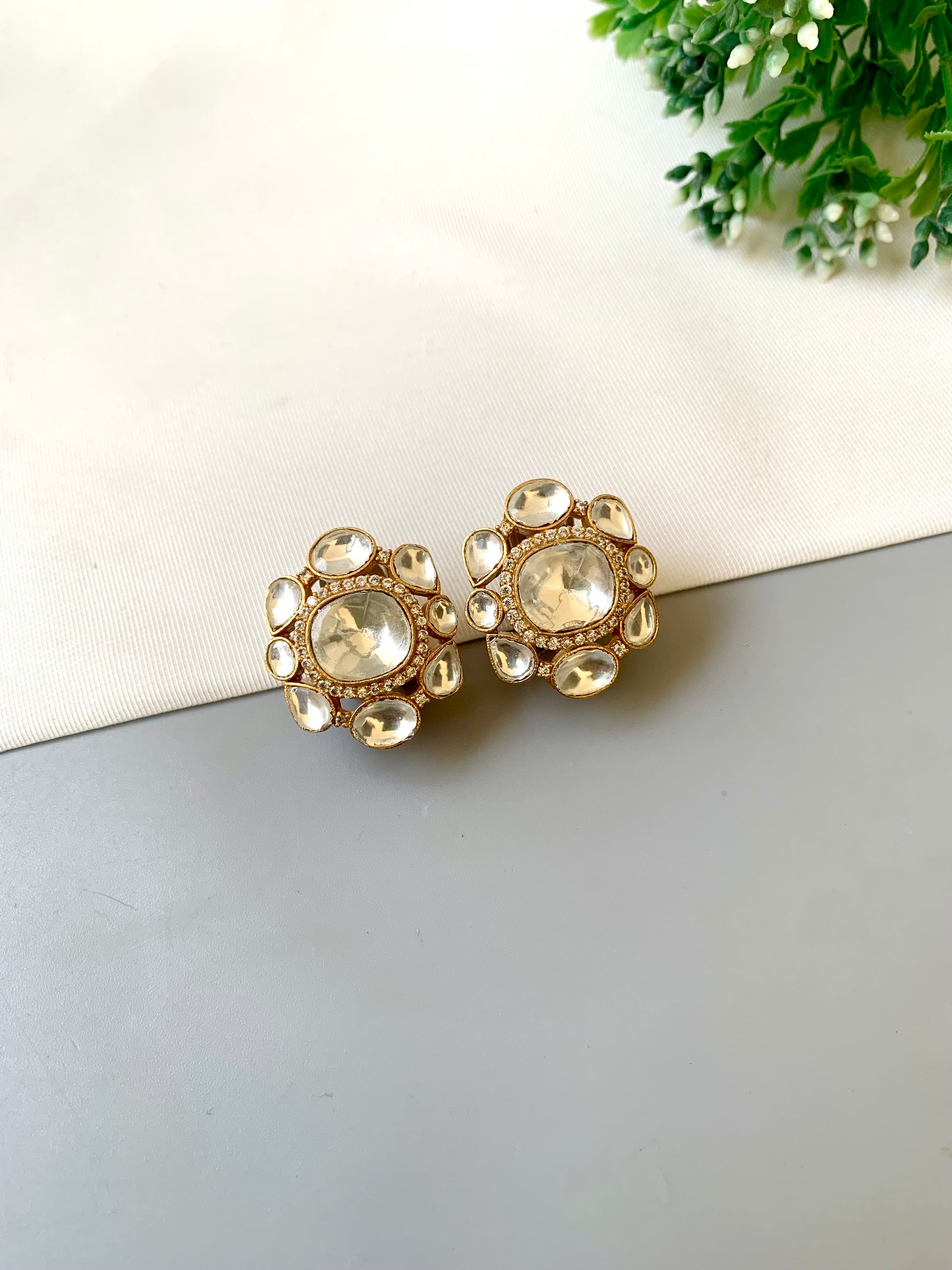 Gold and pearl earrings on a light gray surface with a white card and green leaves in the background