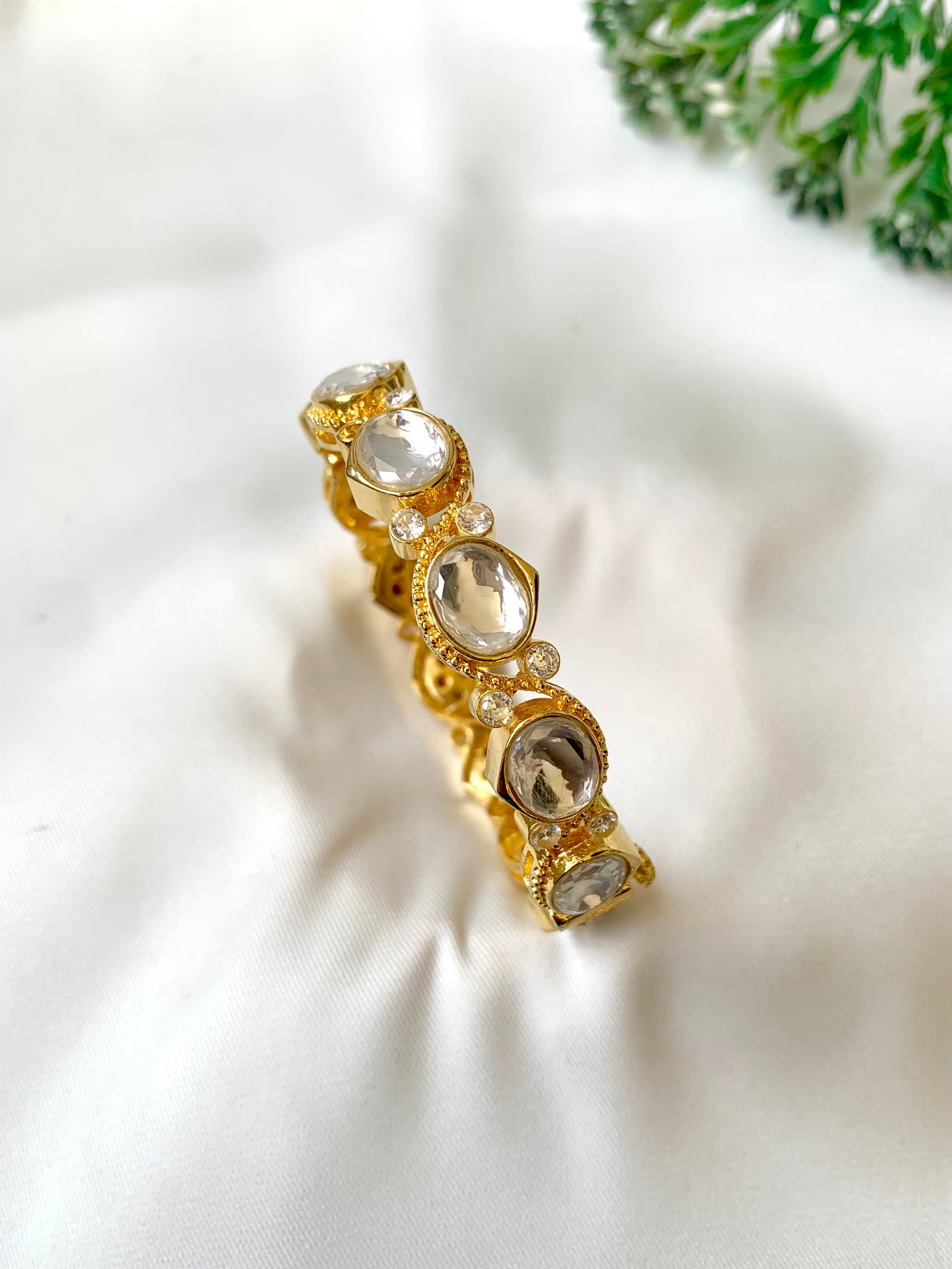 Gold bracelet with clear stones on a white fabric background