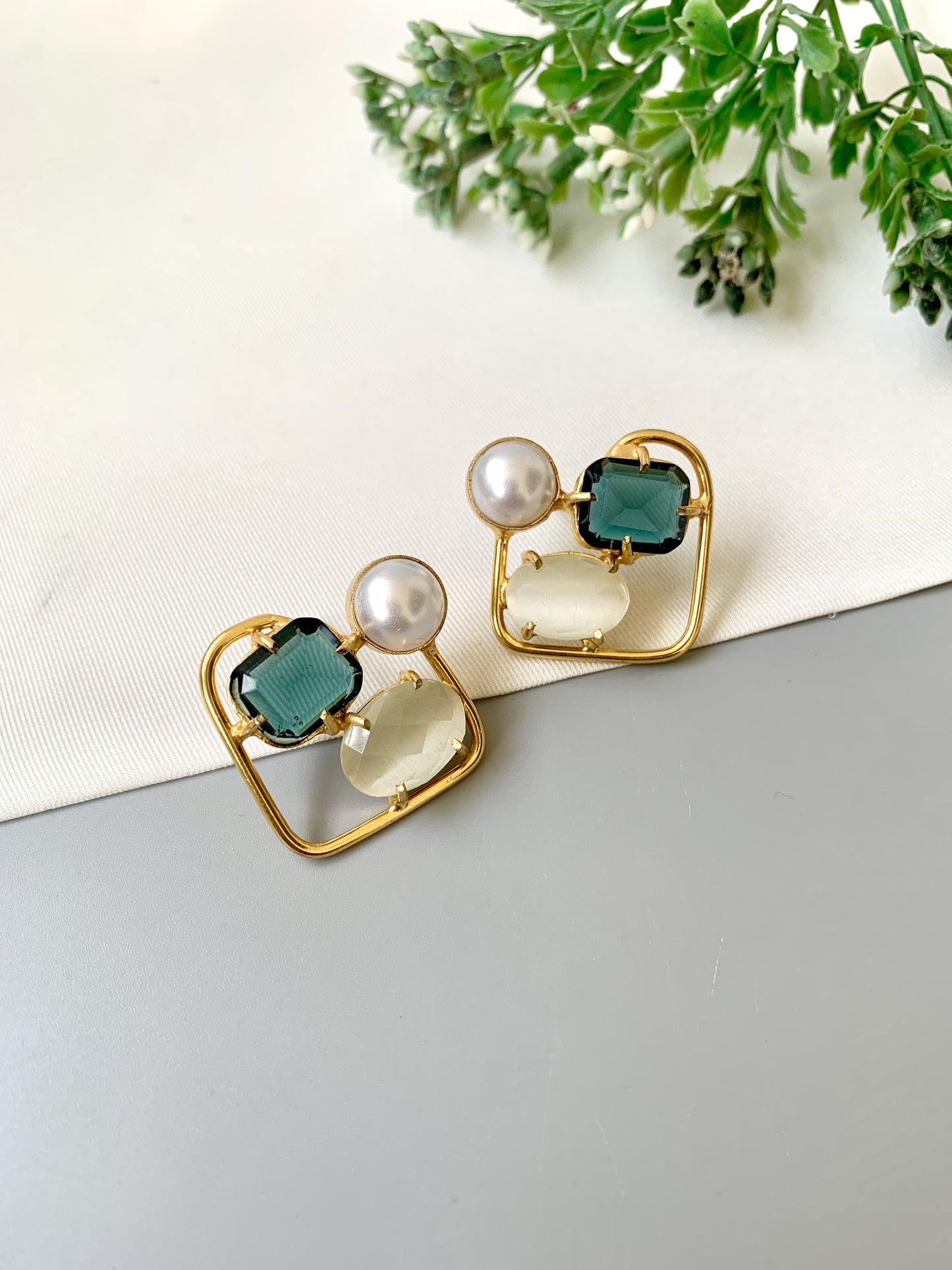 Pair of earrings with green, pearl, and clear stones on a light background