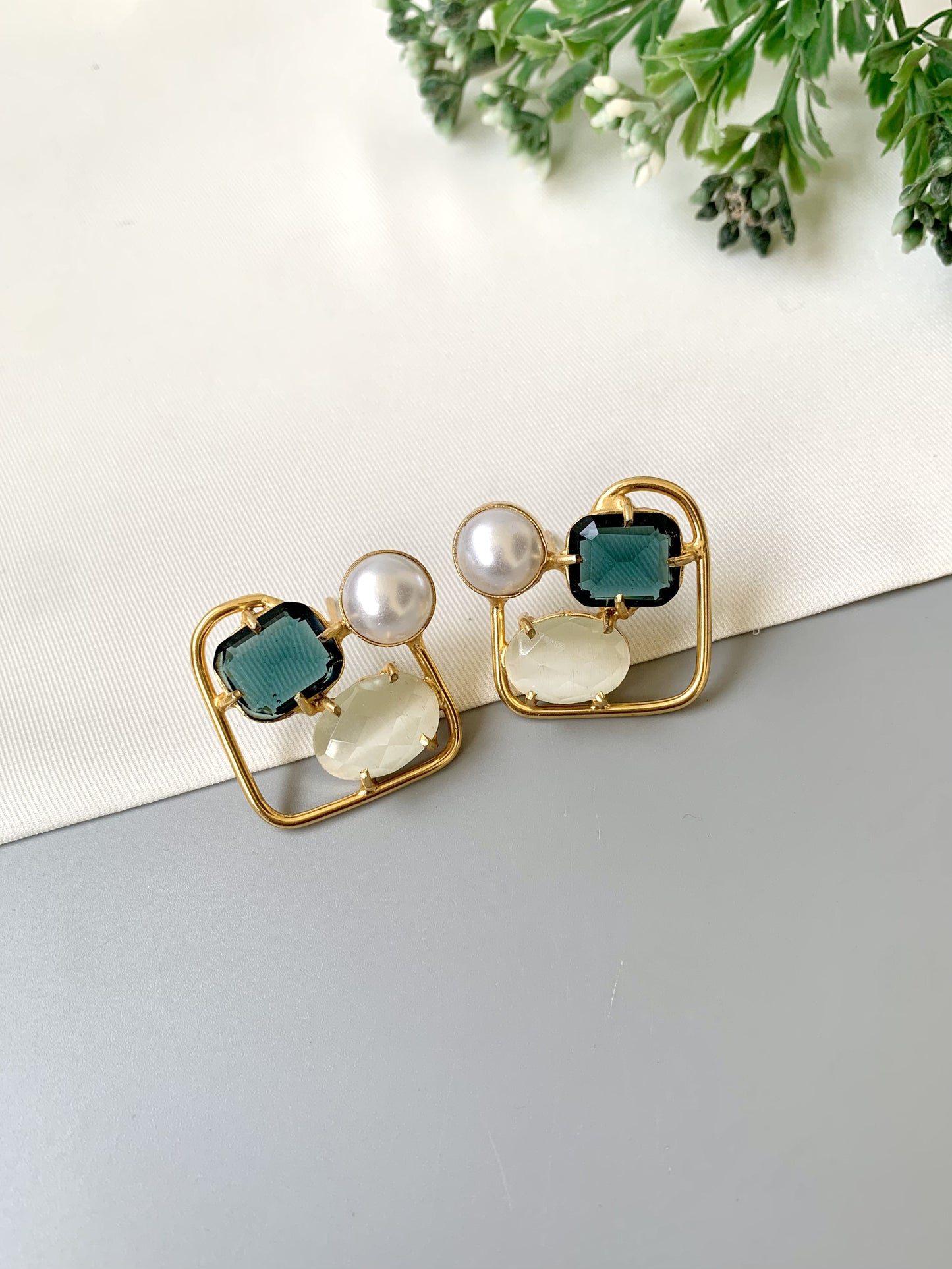 Gold earrings with green and white stones on a light background
