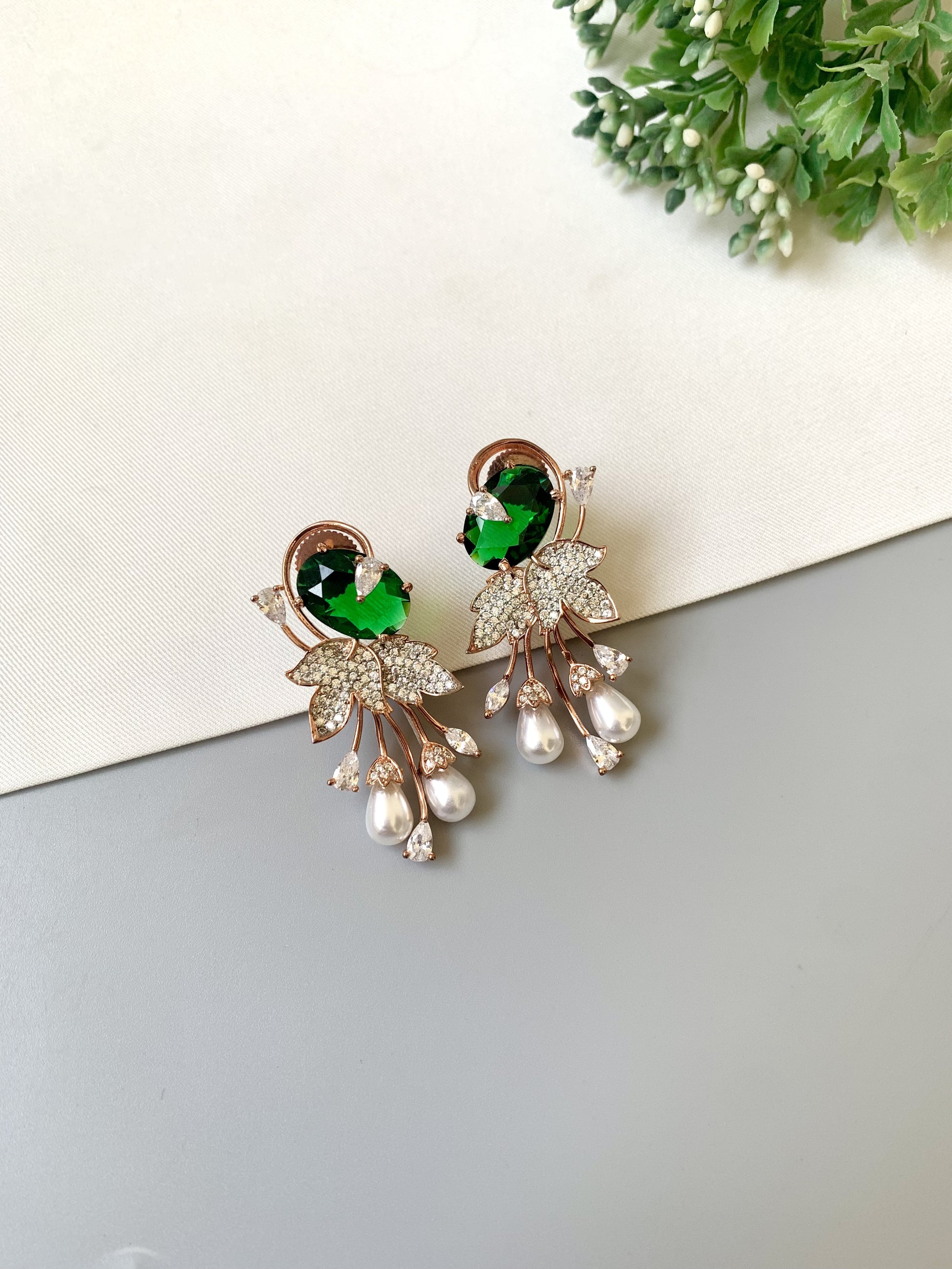 Earrings with green gemstones and pearl-like elements on a light background