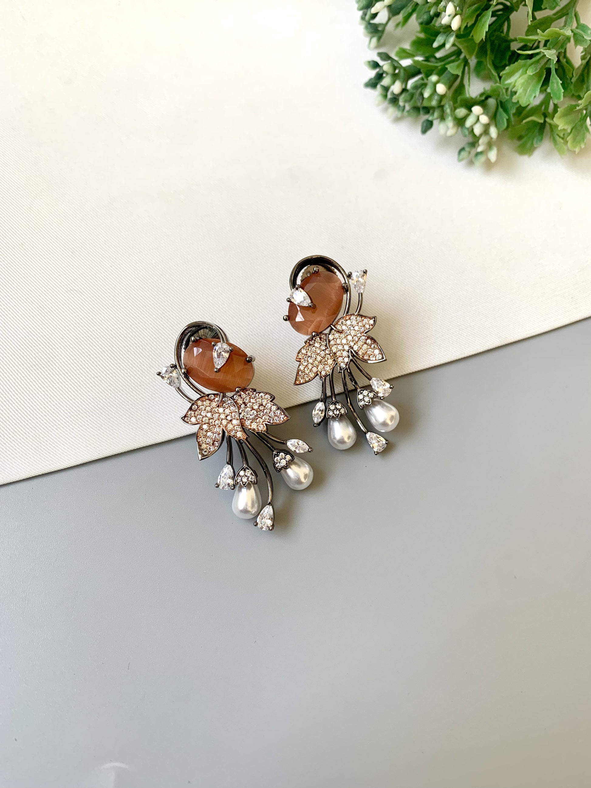 Pair of ornate earrings with gemstones and pearls on a reflective surface.