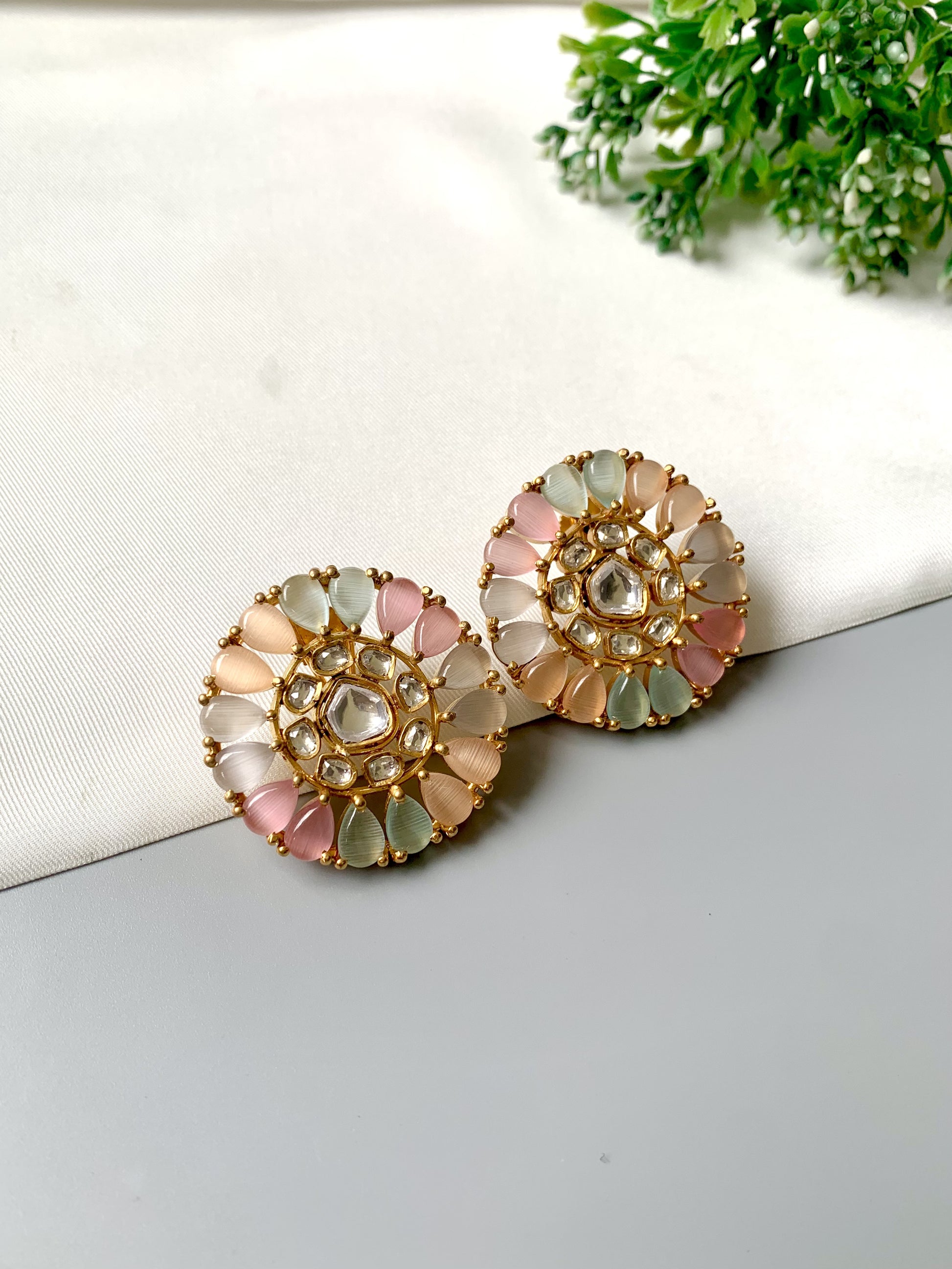Pair of decorative earrings on a white surface with a plant in the background