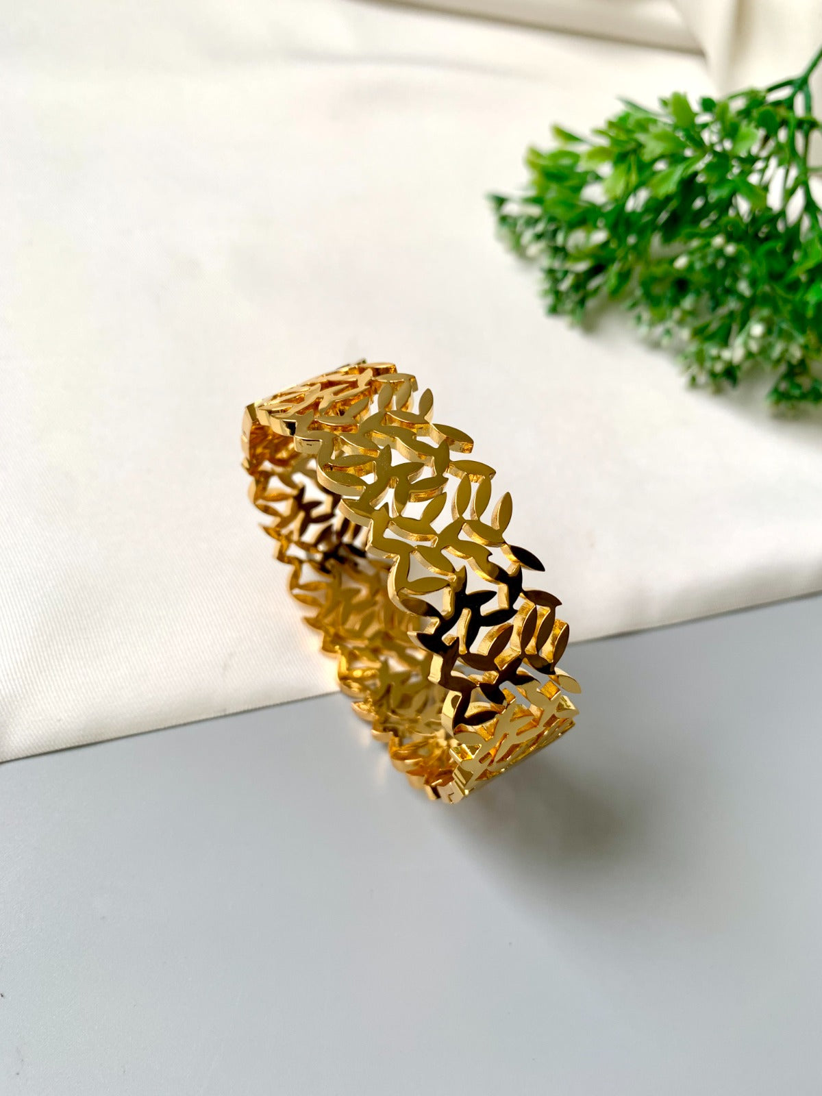 Gold bracelet on a white fabric background with greenery