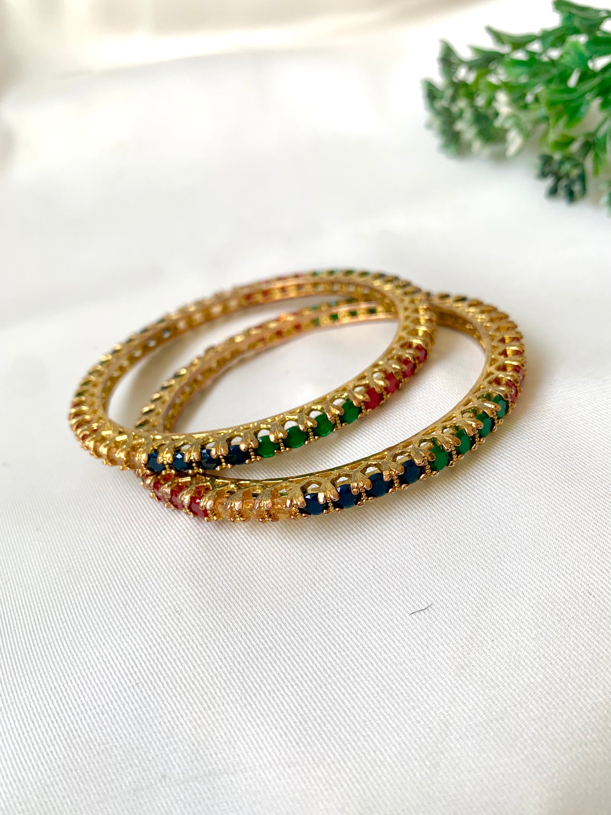 Set of gold bangles with multicolored stones on a white surface
