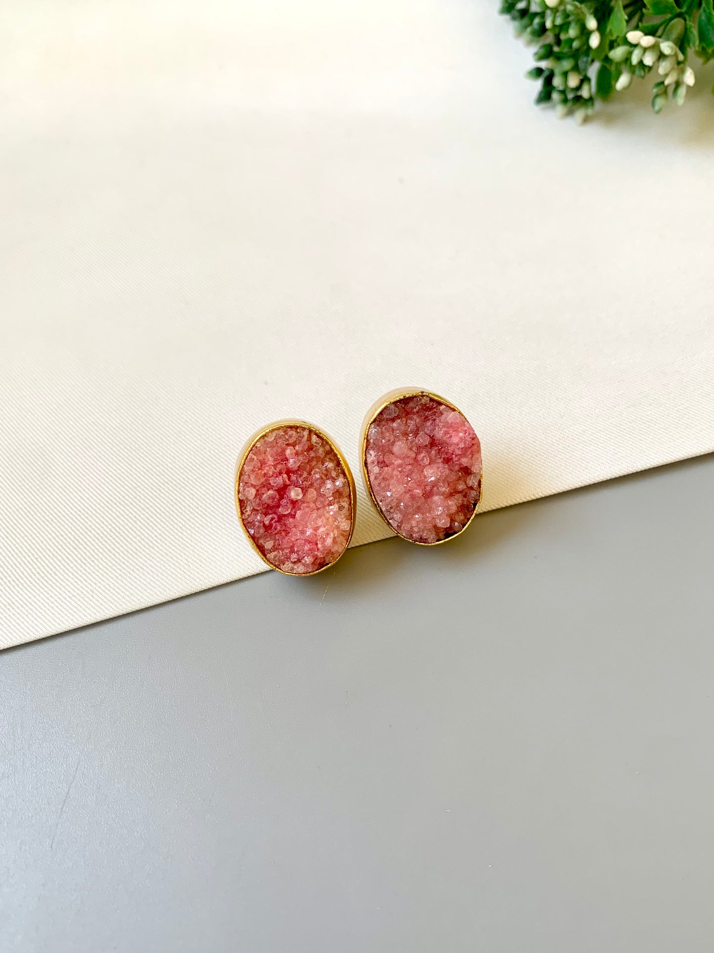 Pink druzy earrings on a light surface with greenery in the background