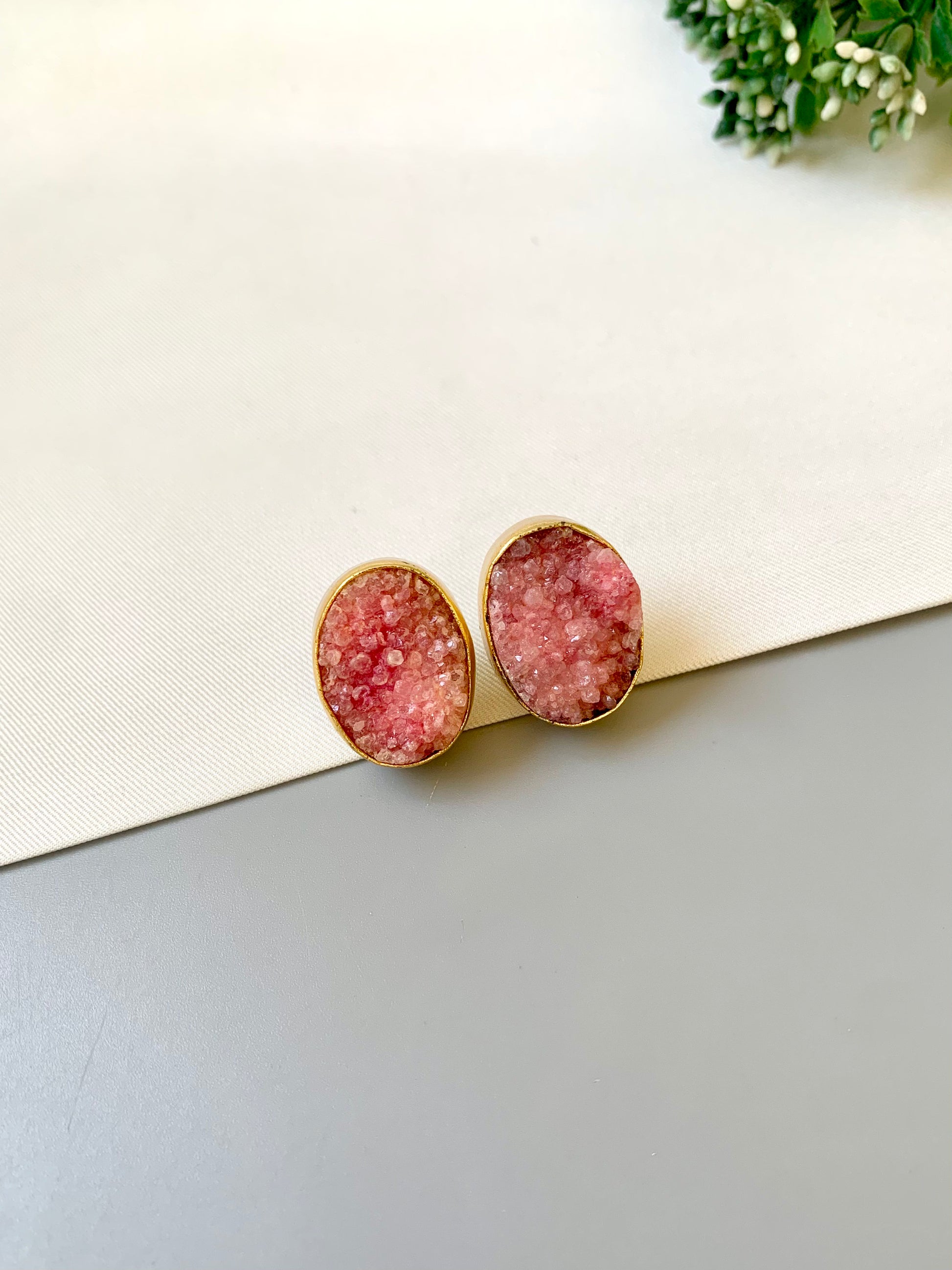 Pink druzy earrings on a light surface with greenery in the background