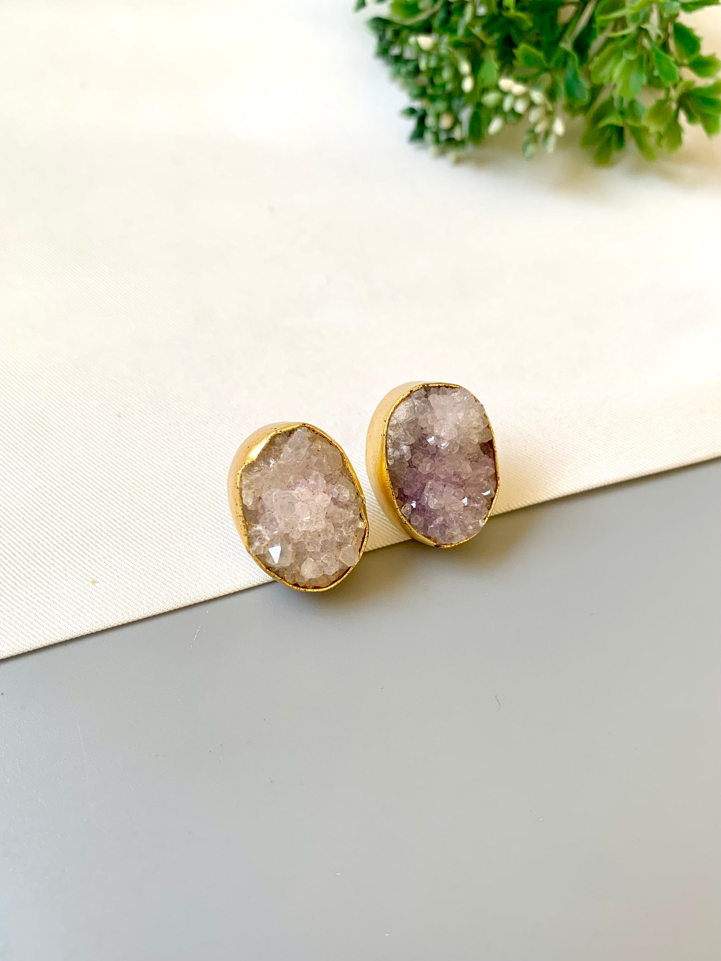 Gold earrings with druzy stones on a light surface with greenery in the background