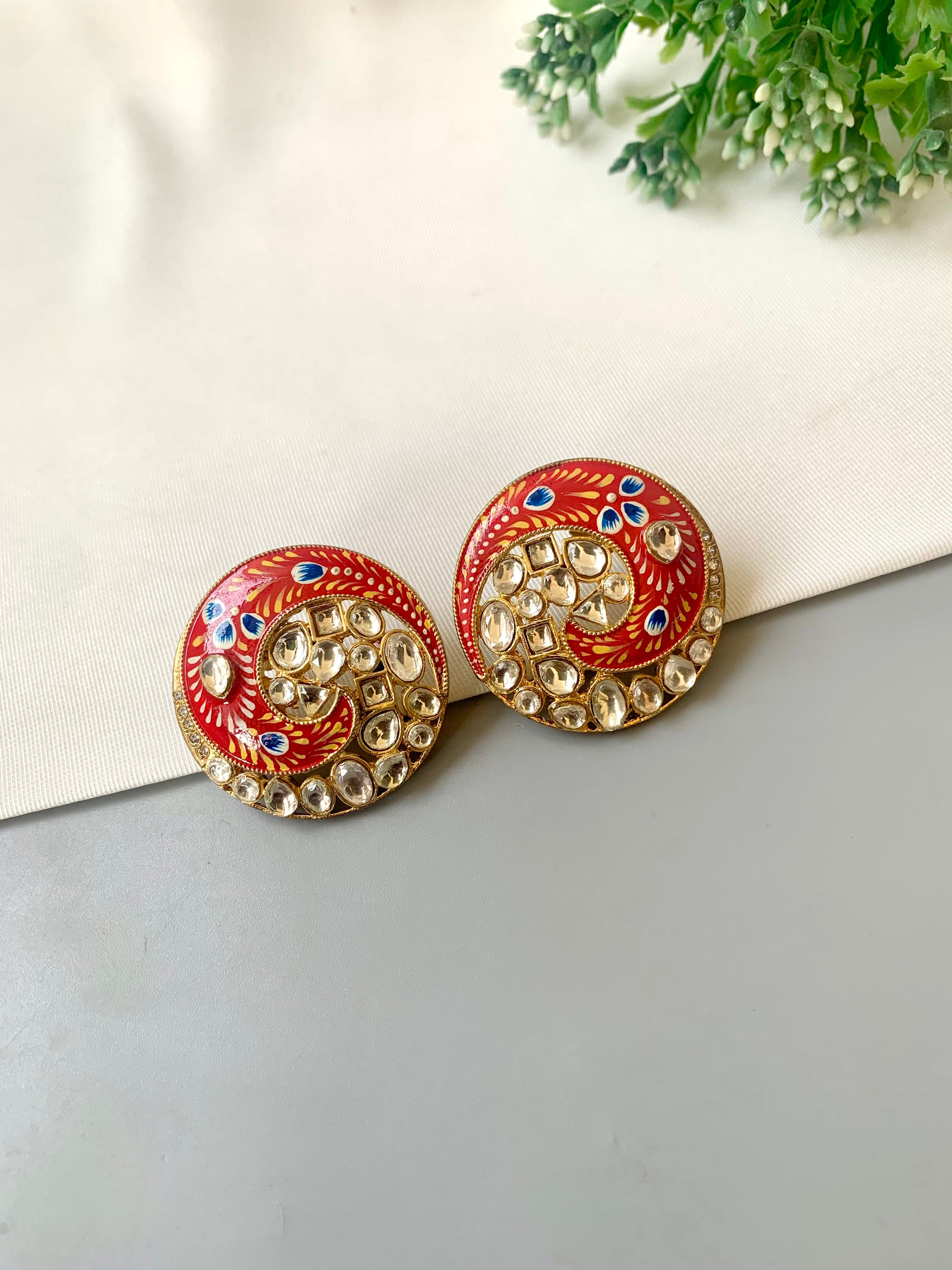 Pair of decorative earrings on a light surface with greenery in the background