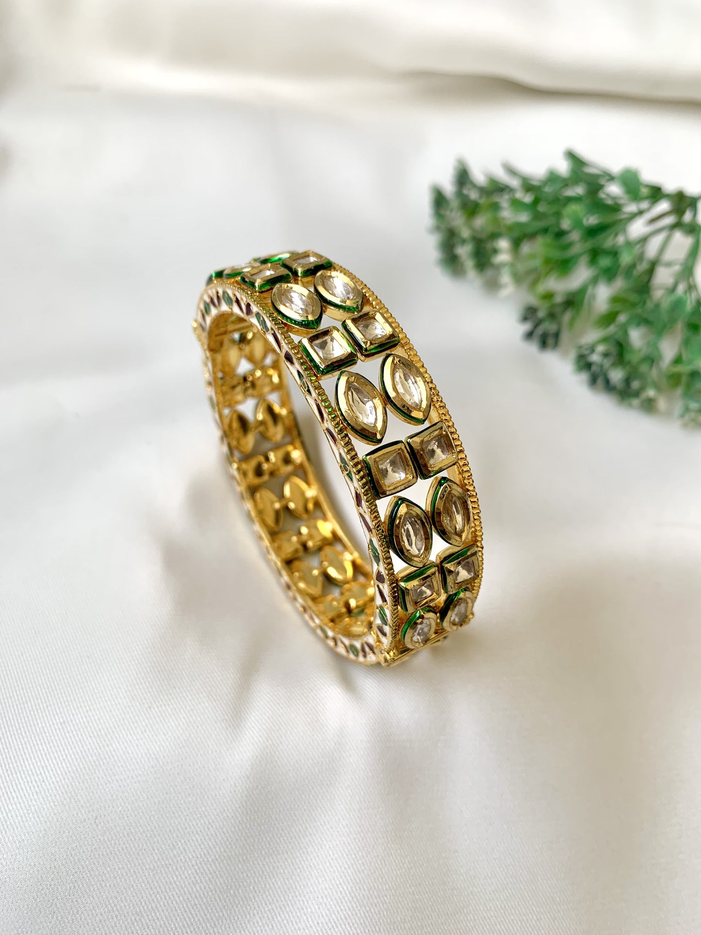 Gold bracelet with green accents on a white fabric background