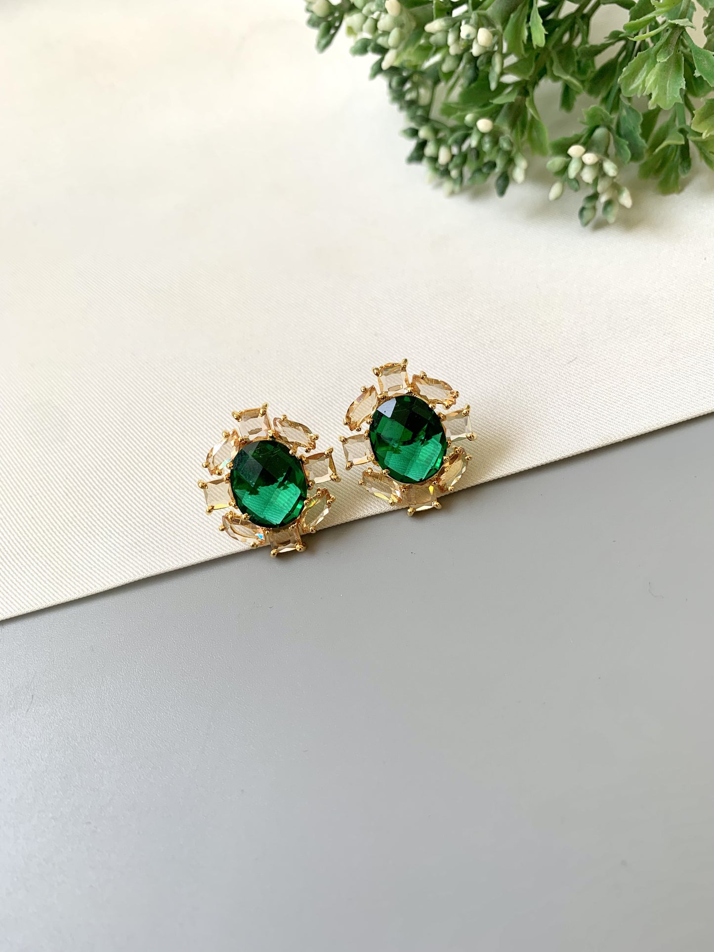 Green gemstone earrings on a light surface with greenery in the background