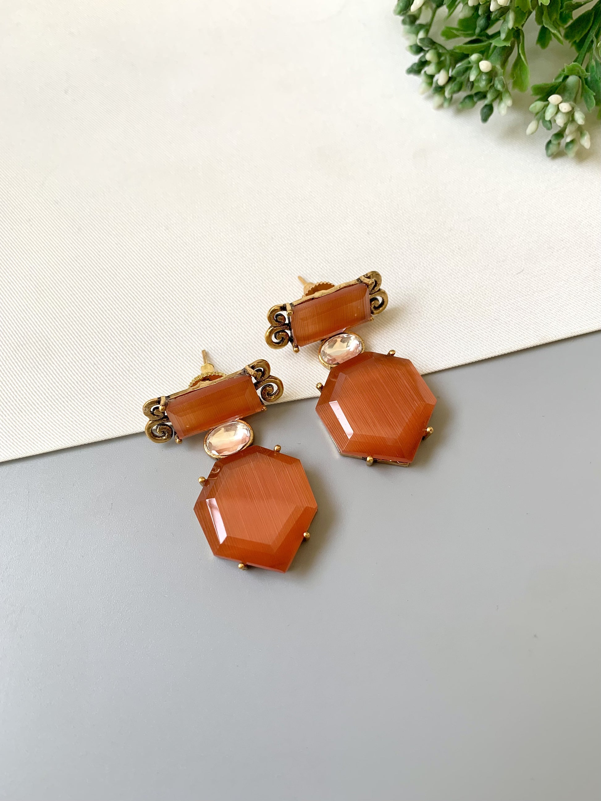 Pair of orange hexagonal earrings with gold accents on a light gray surface.