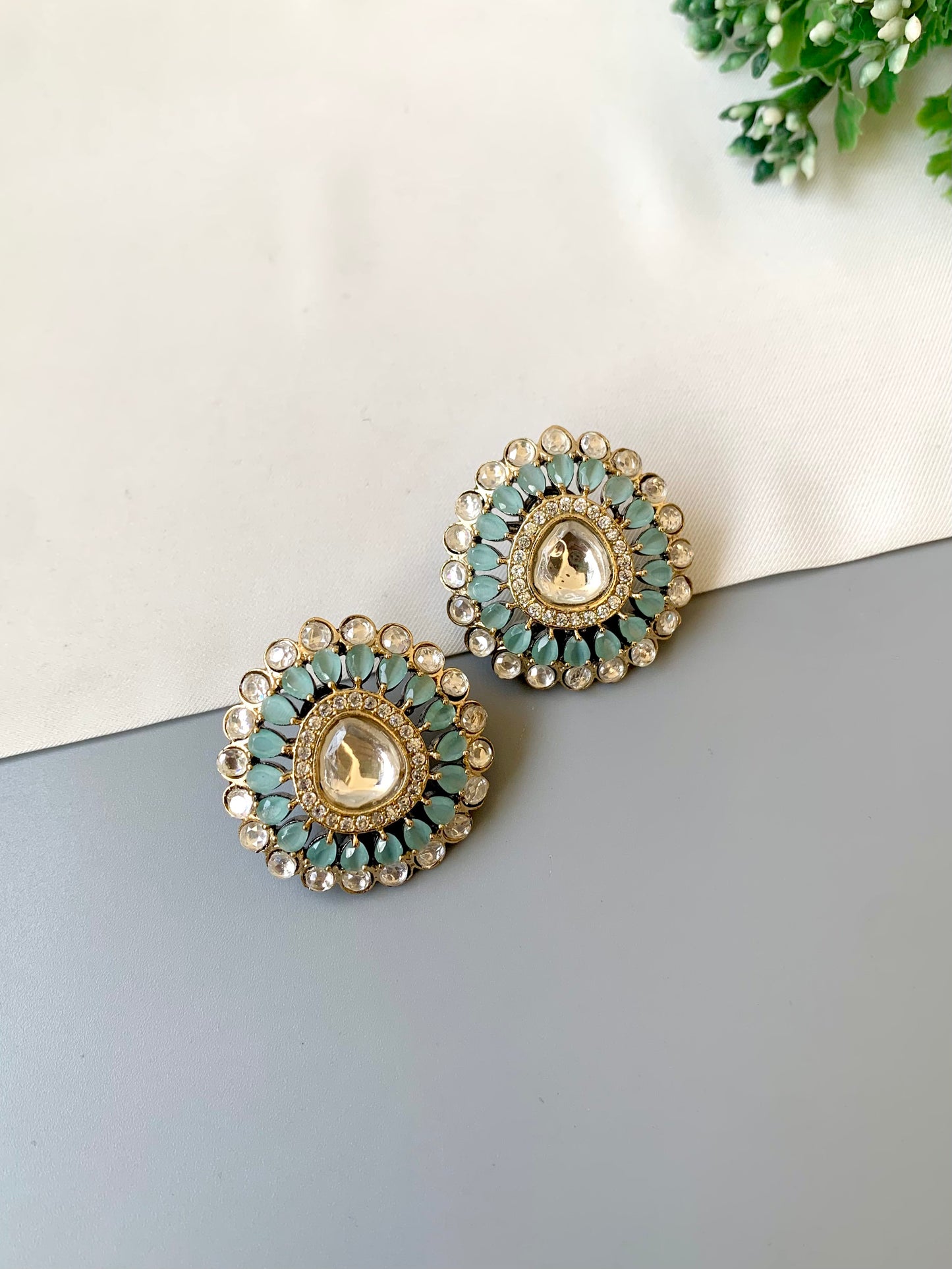 Pair of decorative earrings with green and gold details on a light gray surface.
