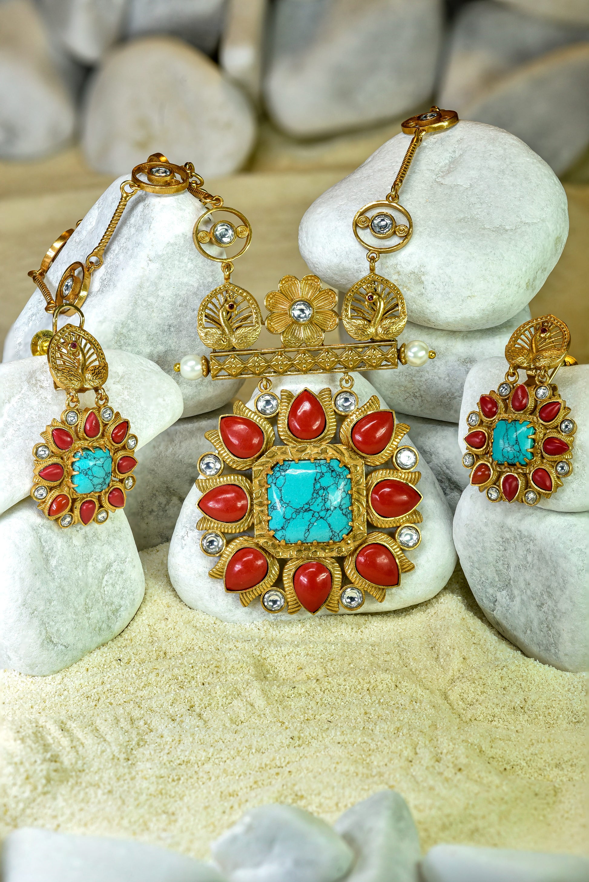 Ornate jewelry set with turquoise and red stones on pebbles