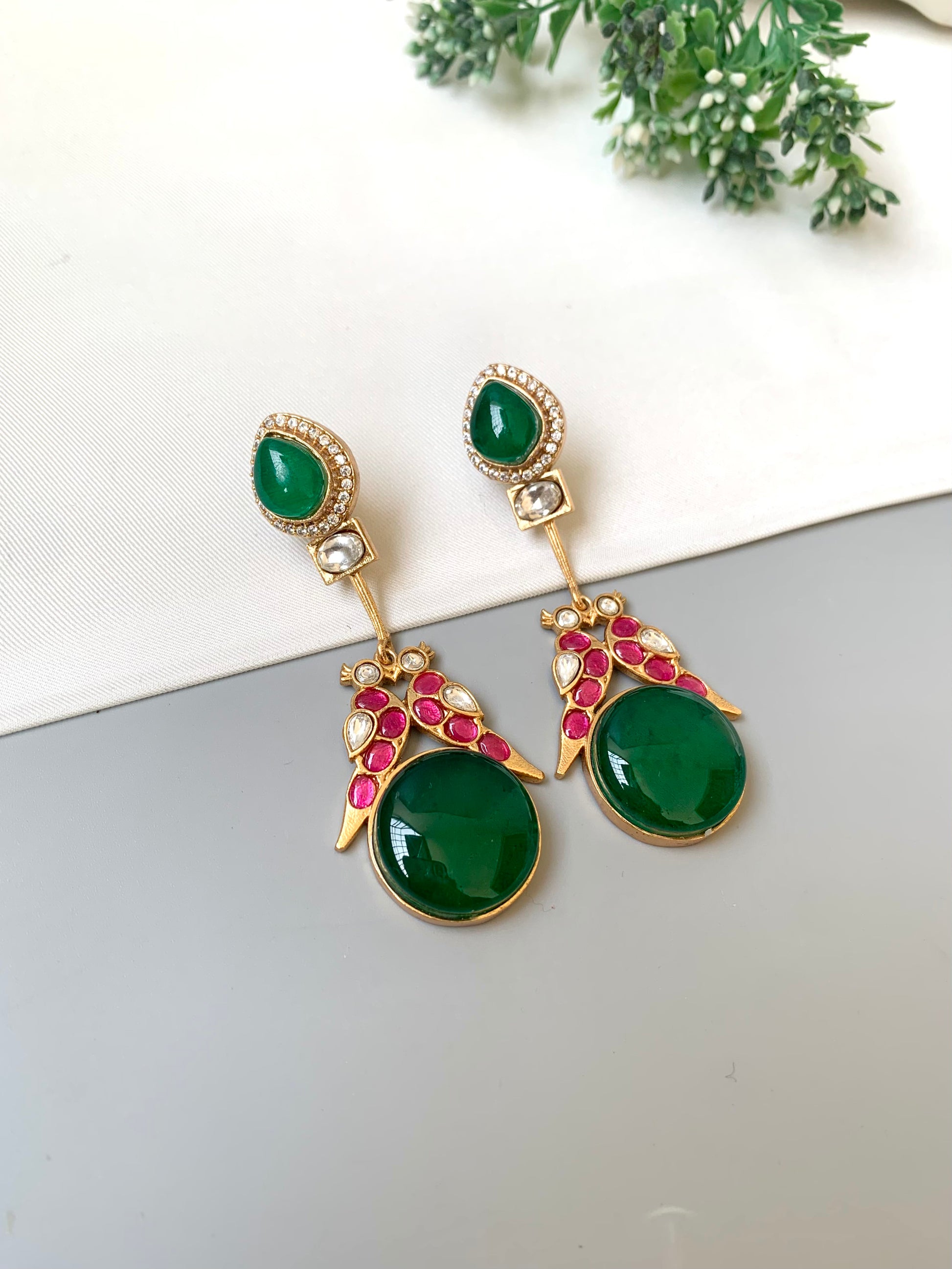 Green gemstone earrings with gold and red accents on a light background