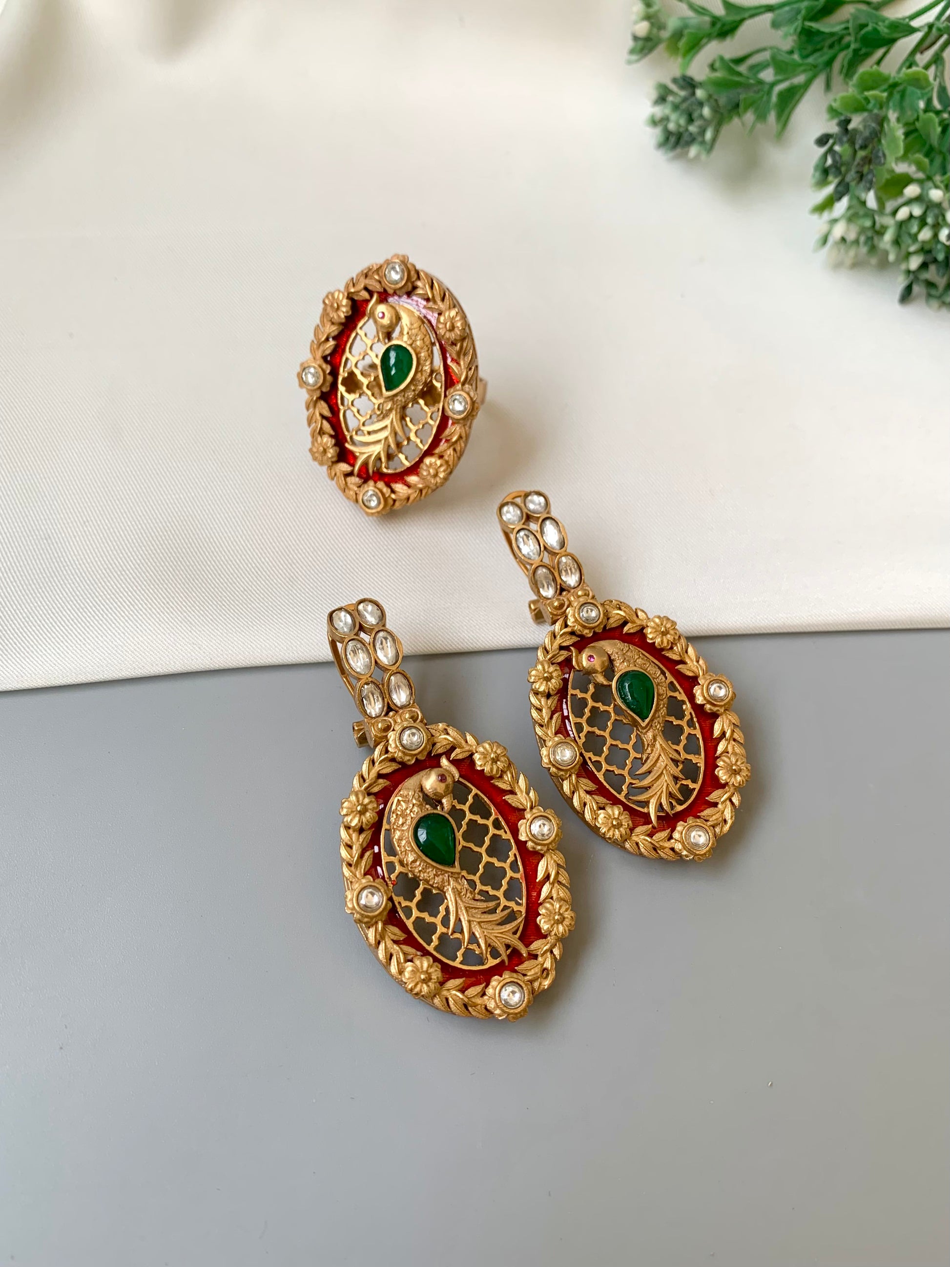 Gold earrings with green and red accents on a light gray surface.