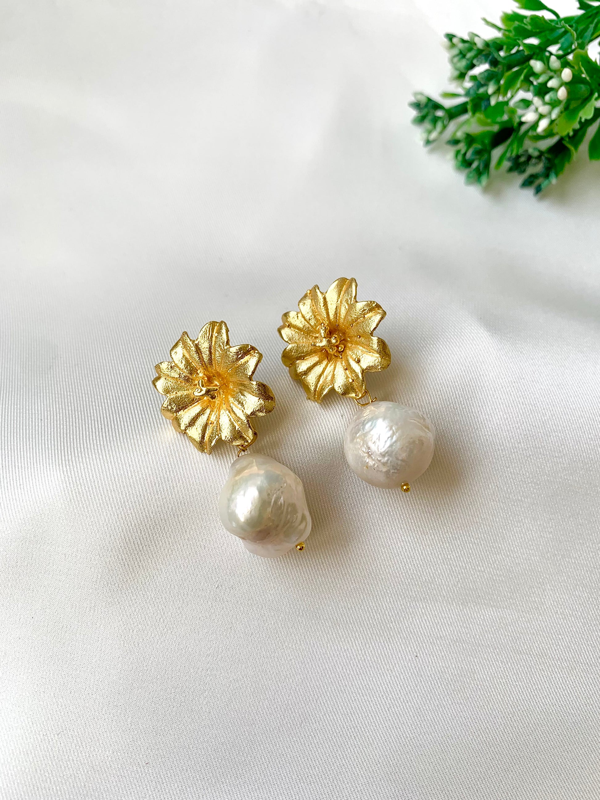 Gold flower-shaped earrings with pearl drops on a white background