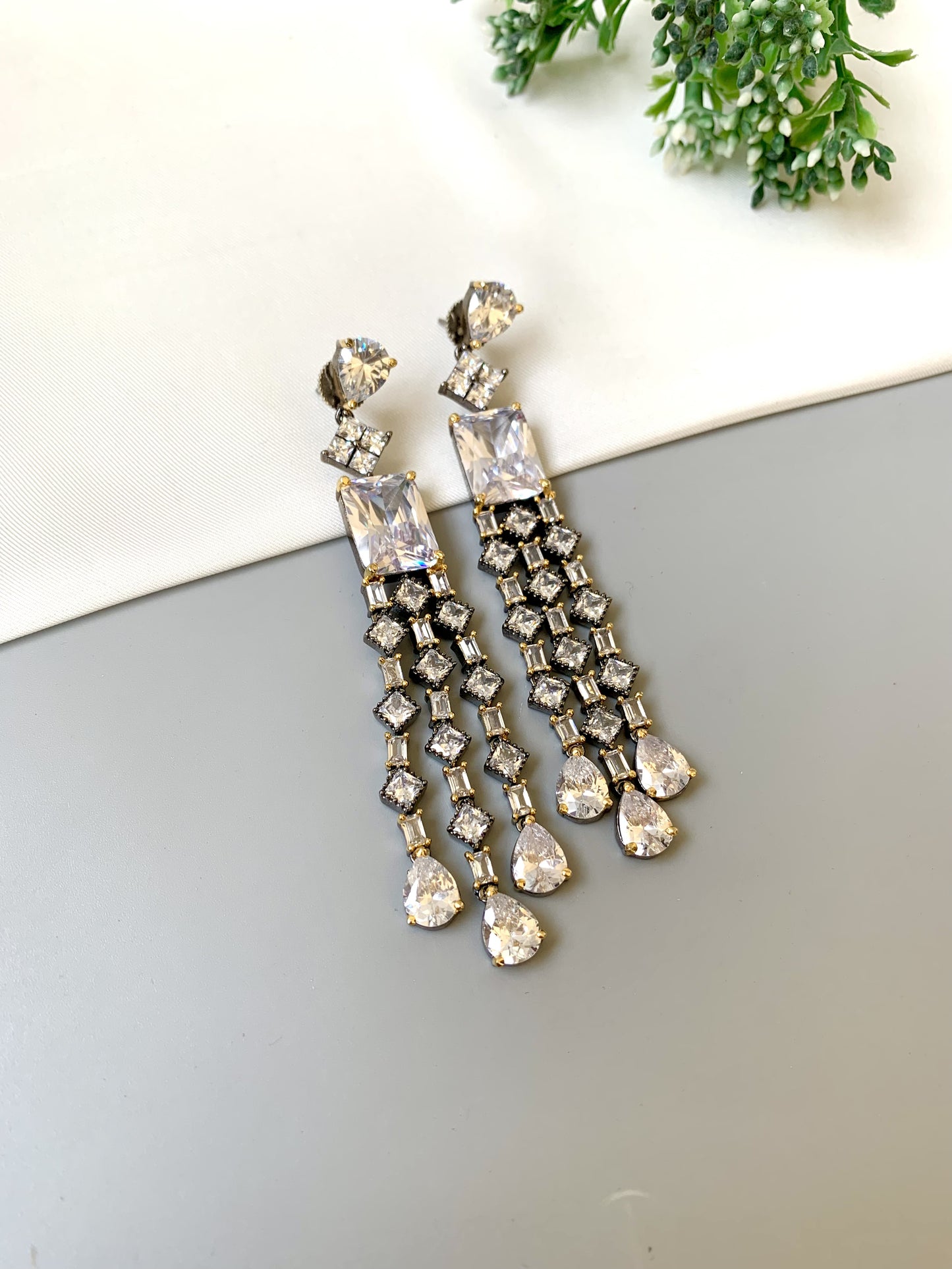 Pair of silver chandelier earrings on a light gray surface with greenery in the background.